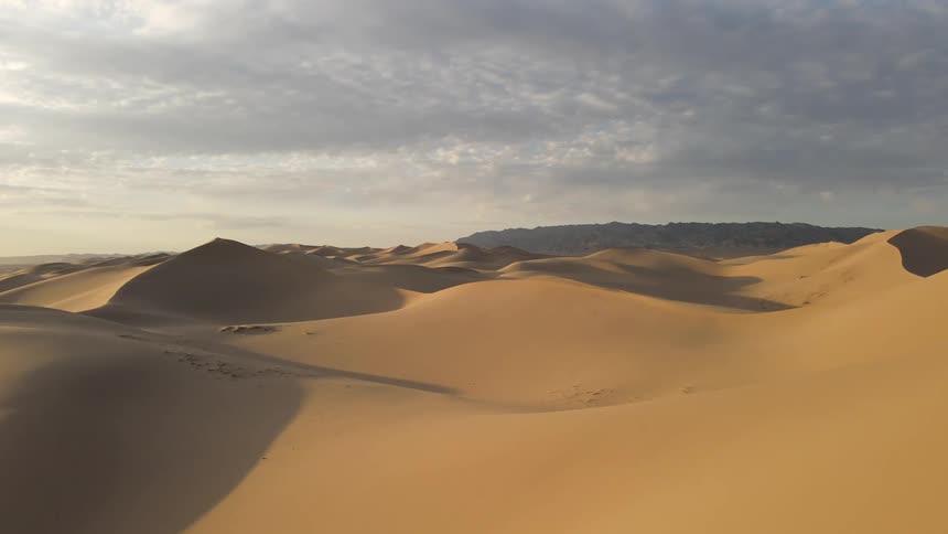 Sunlight shines on the desert dunes under a cloudy sky