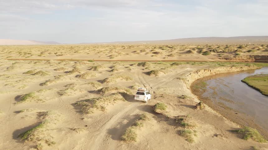A car is driving through the desert near a river