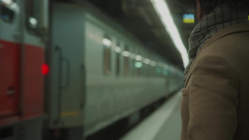 Man standing at a train station with a train passing by