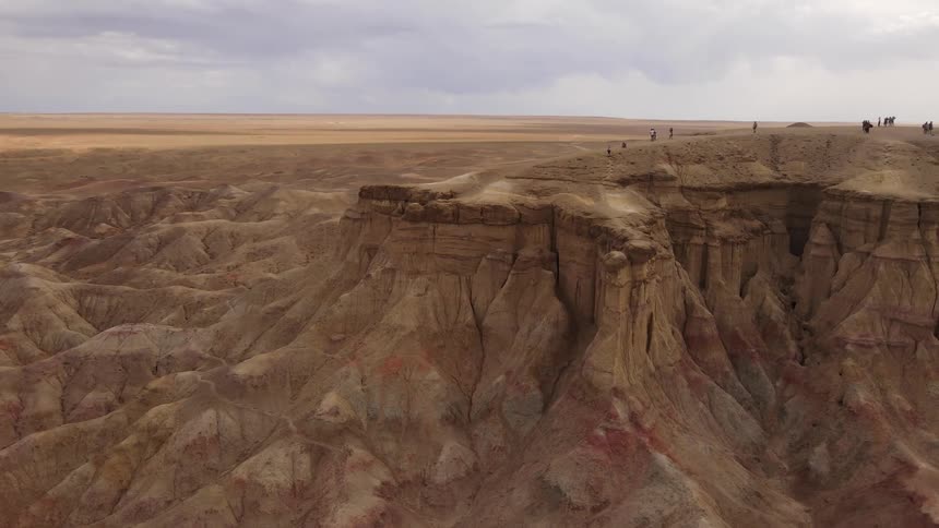 A vast rugged landscape with people exploring the edges of a cliff