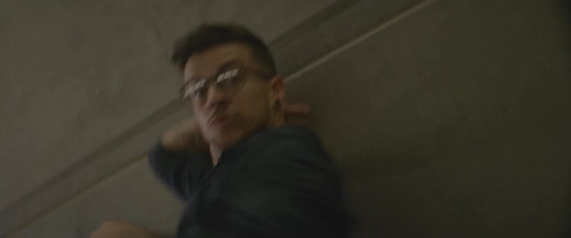 Man in glasses dances close to a concrete wall