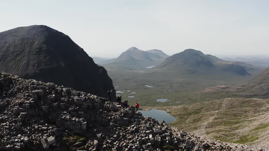 Mountaineers stand on the slope of a mountain looking at the valley