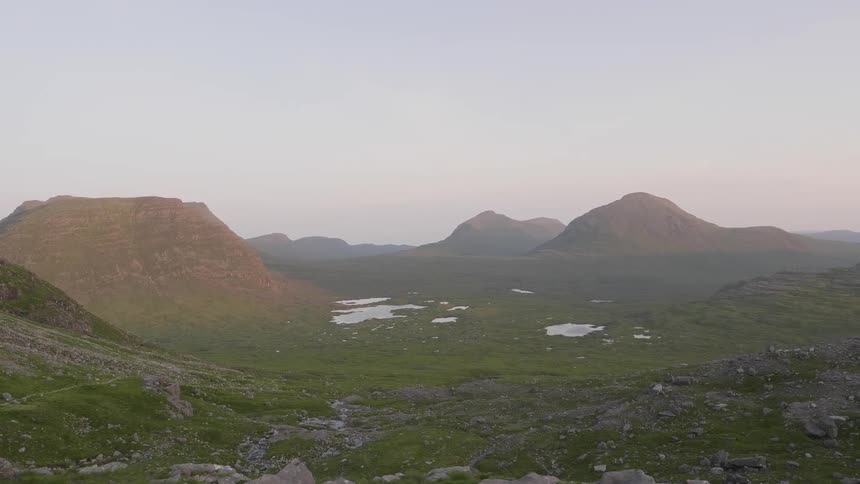 Highland valley surrounded by hills with pools of water surrounded by green moss on a cloudy hazy day
