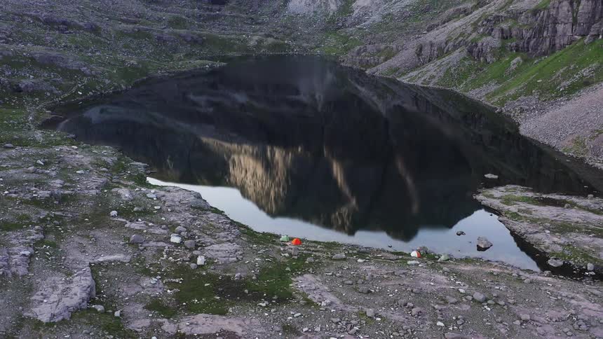 Colorful tents on the shore of a lake reflecting a mountain