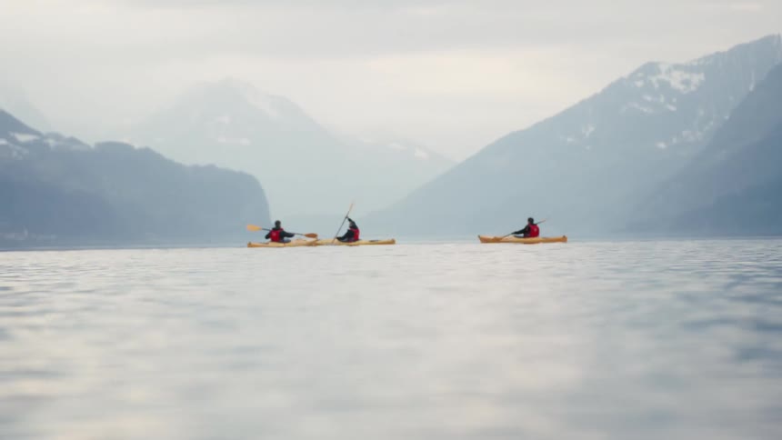 Three kayakers moving through open water with a cloud covered mountain ridge in the background
