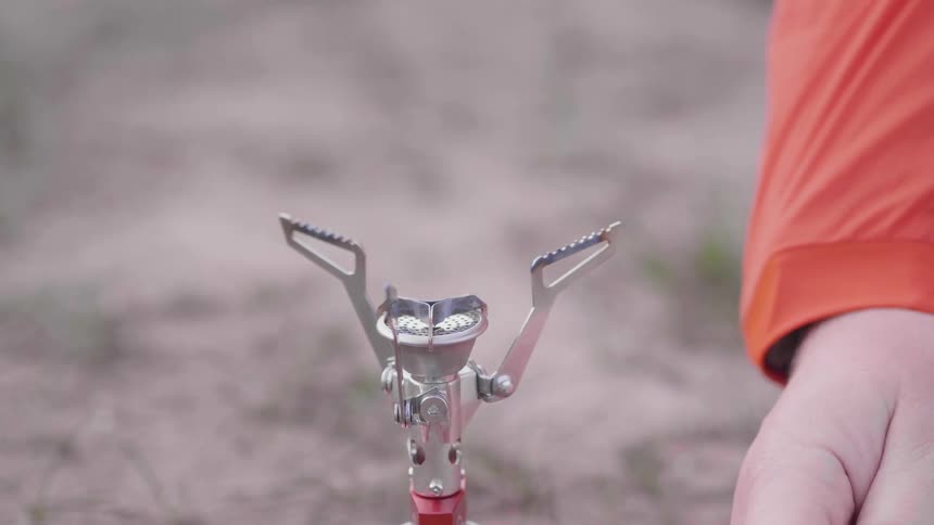 A person lights a camping gas stove to heat water