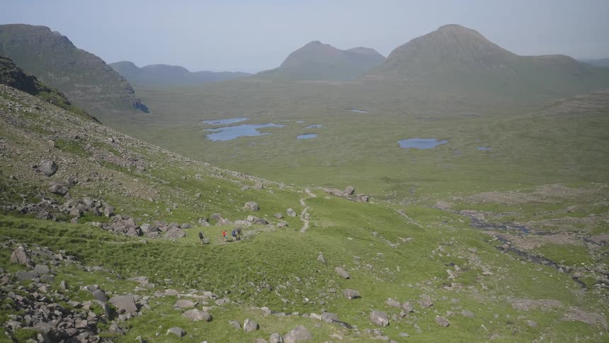 A grassy rocky area near mountains with people hiking on a path