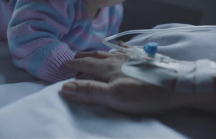 Elderly patient touches hand of young child with her hand attached to an iv