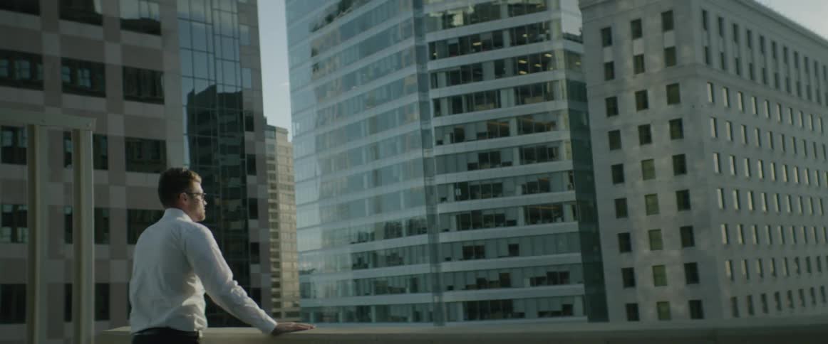 Man standing on a balcony overlooking huge city buildings