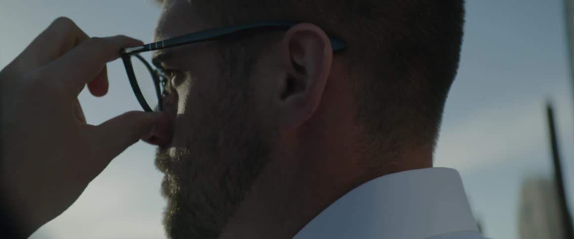A man standing outside puts on eye-glasses