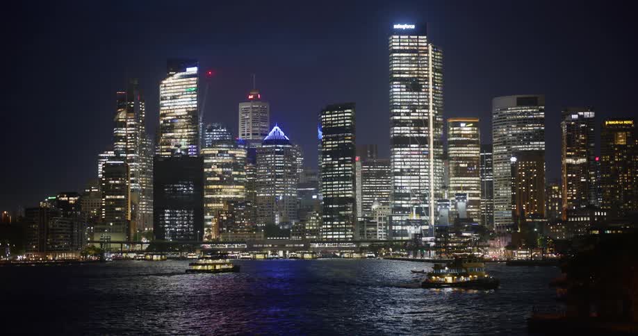 Boats sail through the urban city harbor at night