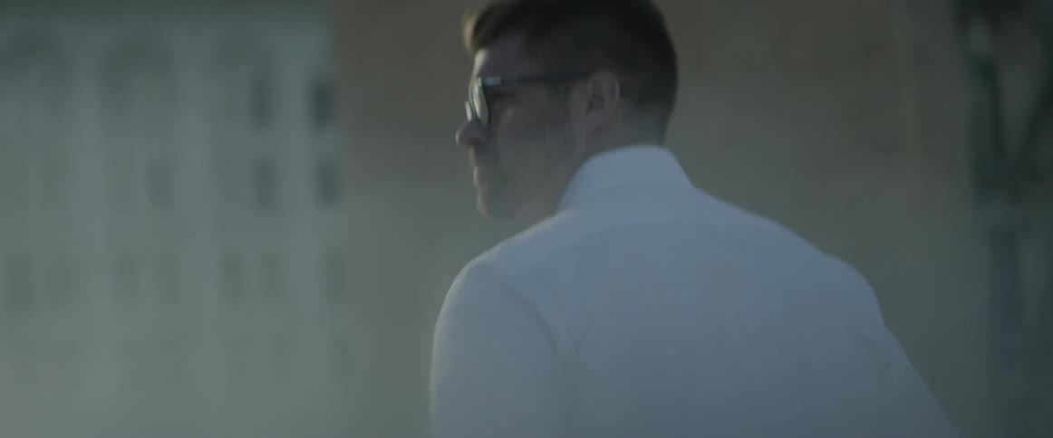 A man in a white button-down shirt is walking in an urban setting