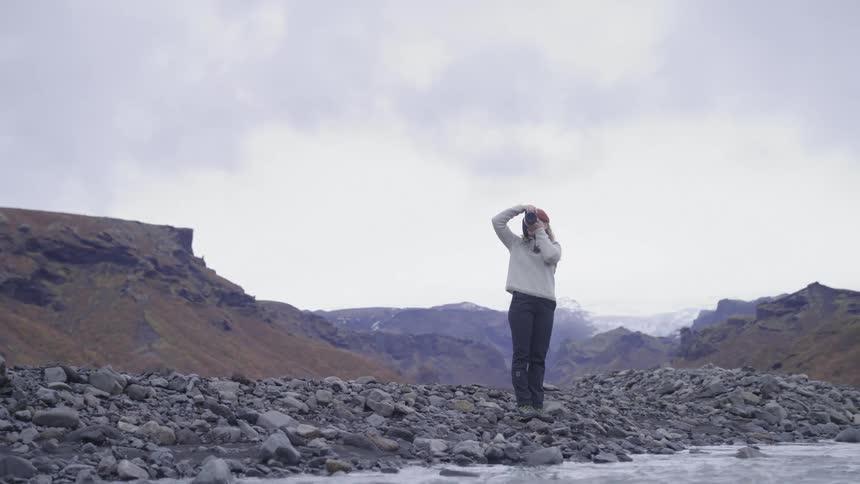 Woman taking photos by a river surrounded by mountains in winter