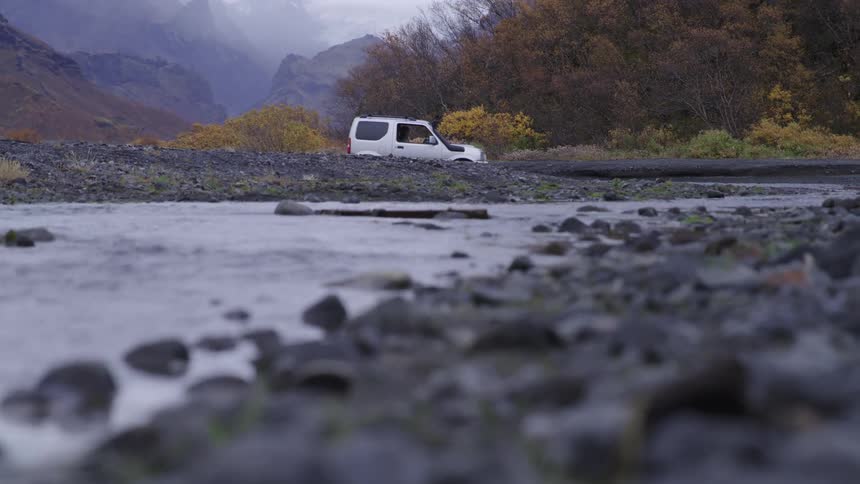 A white vehicle drives on a rocky terrain surrounded by autumn foliage