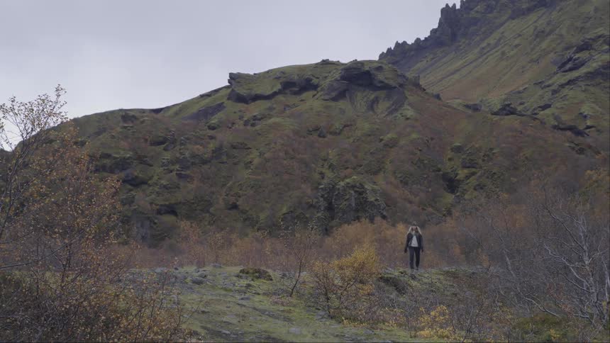 A woman casually strolling across a grassy valley path
