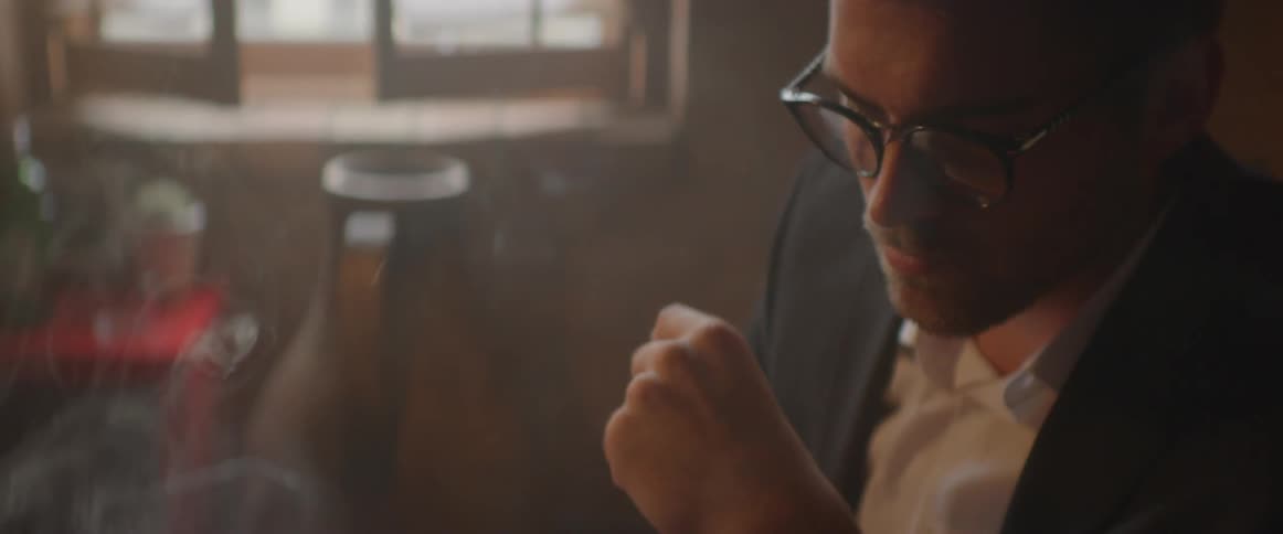 Man wearing glasses at a table has smoke in his face