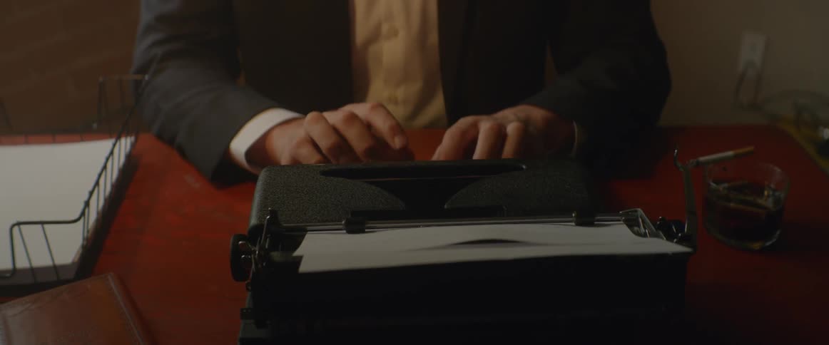 A man sitting at a desk types at a typewriter