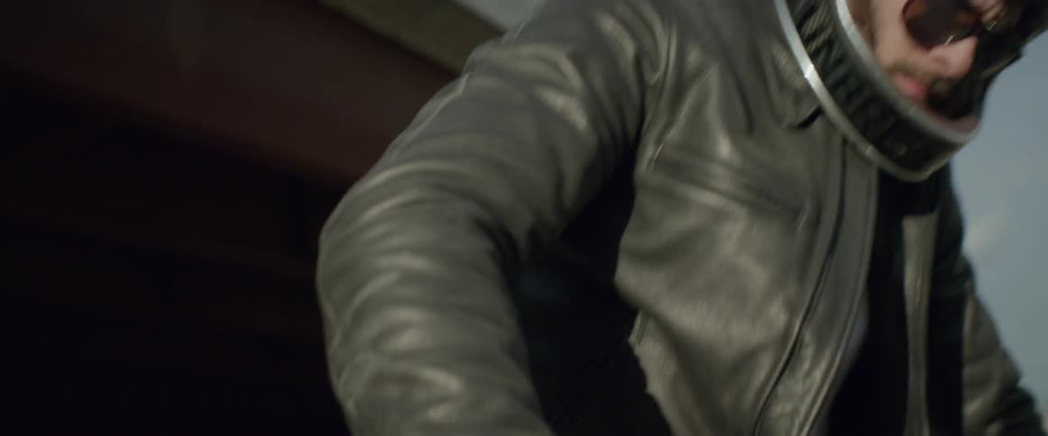 A man wearing a motorcycle helmet and leather jackets sits down on a bike