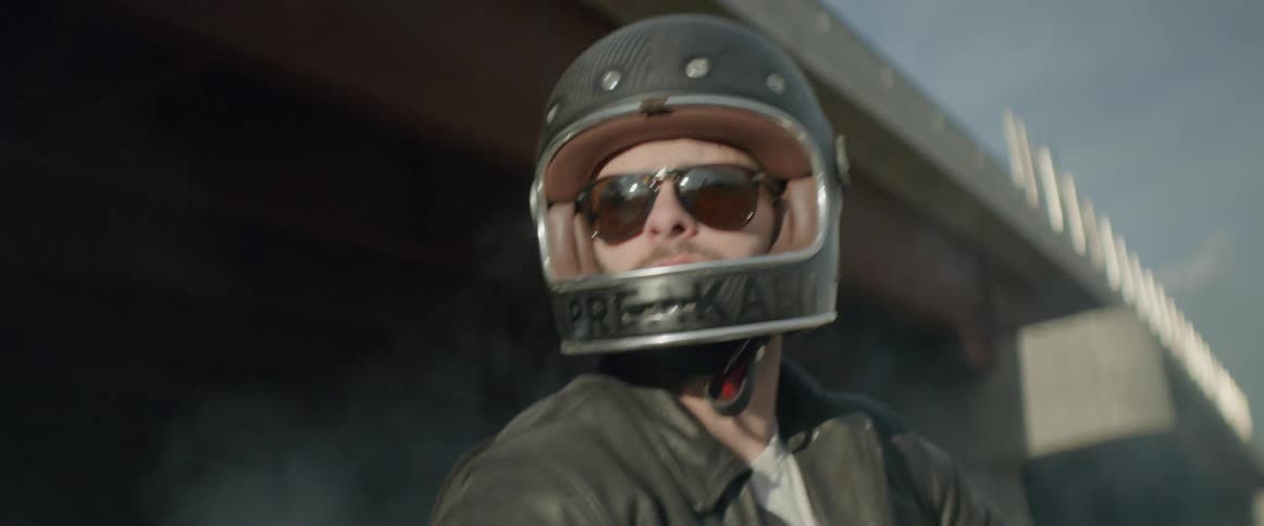 A man wearing a motorcycle helmet sits back by an overpass