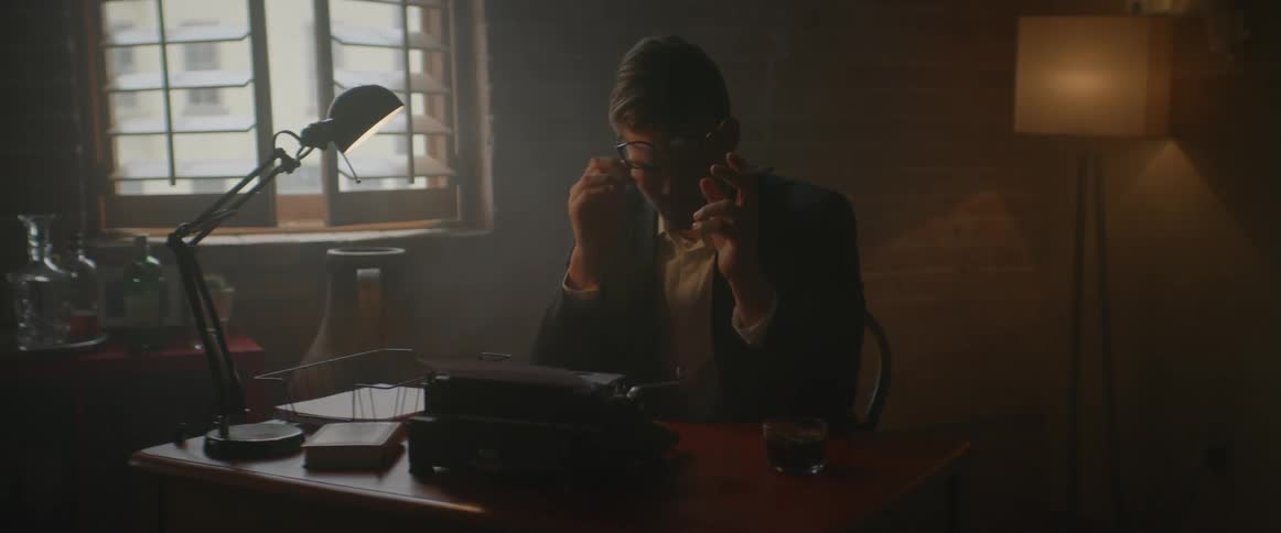 A man rubs his face at a desk holding a cigarette