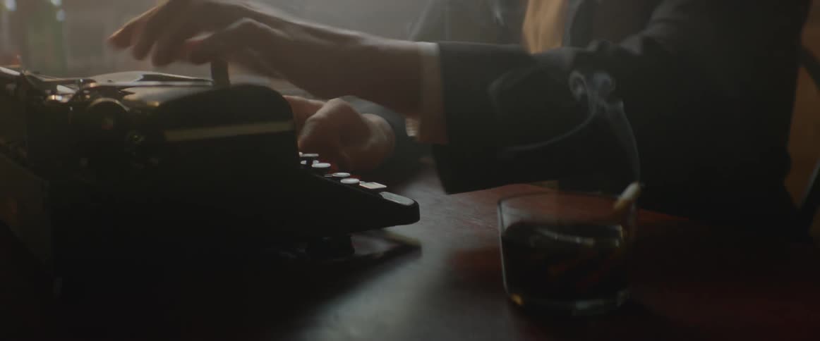 Man in a suit jacket types on an old typewriter