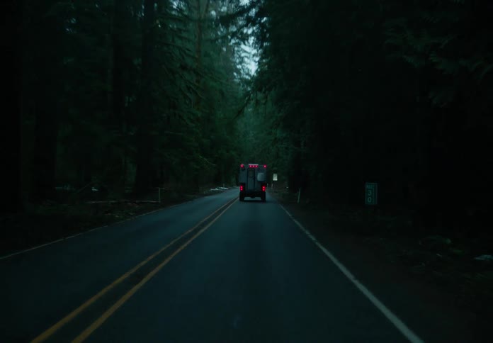 Ambulance driving on a road through a dark forest