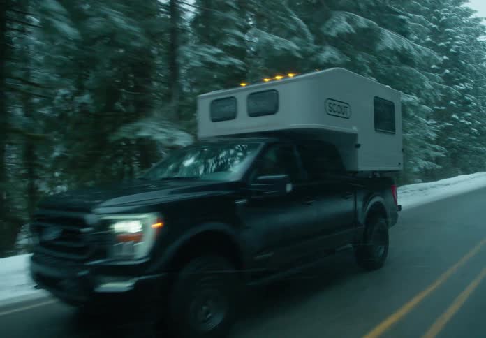 Black pickup truck driving through a snowy forest on a highway