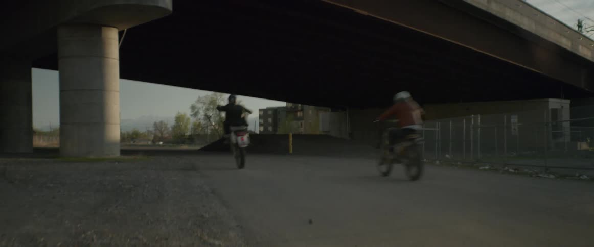 Two people on dirt bikes ride under highway bridge