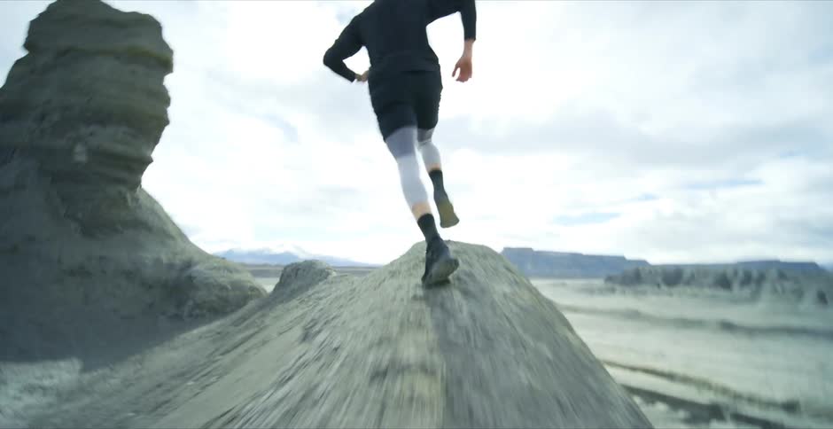 A person is running on a rocky terrain with large rock formations in the background