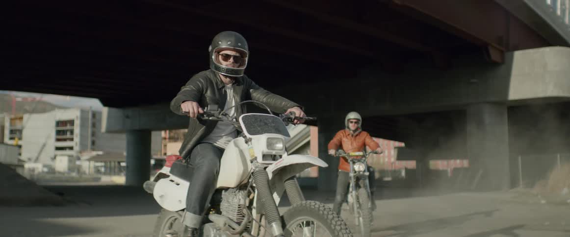 Two motorcyclists sit on their bikes under a freeway pass