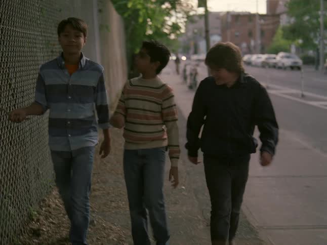 Three young boys walking down a street and talking with each other