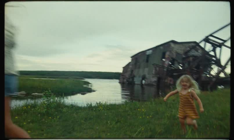 A big girl running and a little girl running after her and smiling in a field of grass near a lake
