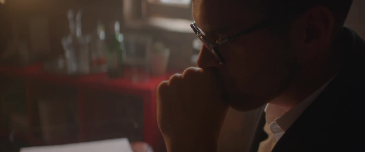 A man sits at a desk with his hand to his mouth