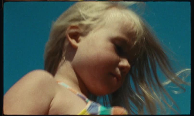 A little blonde girl is standing and her hair is moving in the wind
