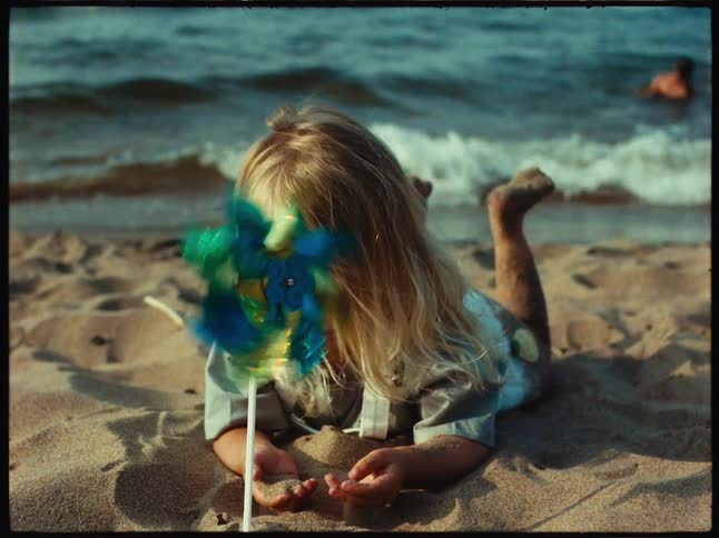 A colorful pinwheel spins in front of a girl playing in a sandy beach