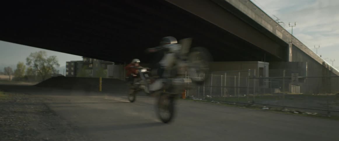 Two people do wheelies racing under an overpass