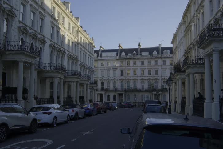 A street with many parked cars and a large building with old architecture