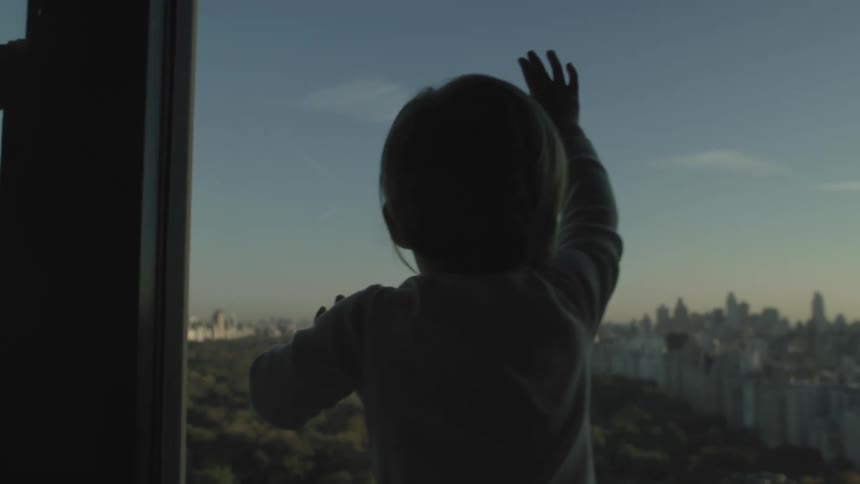 Toddler looking at central park from the apartment window at morning