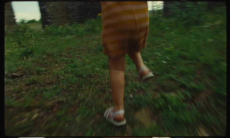 Legs of a child running on grass behind an adult during the day