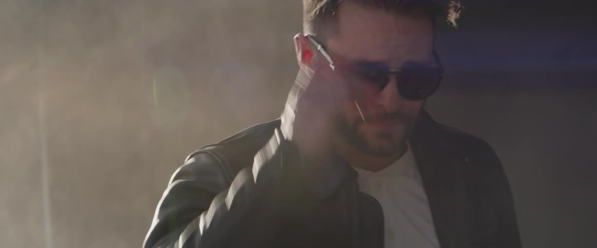 A man takes off his motorcycle helmet, puts on sunglasses and looks around