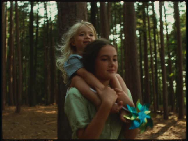 A teenage girl carrying a toddler on her shoulders through a forest