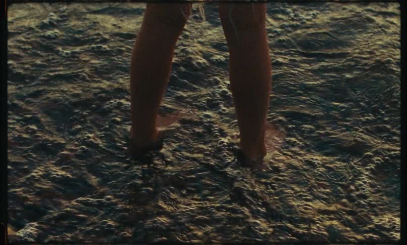 A small person is standing on the edge of the sea and his legs are being wet by the small waves