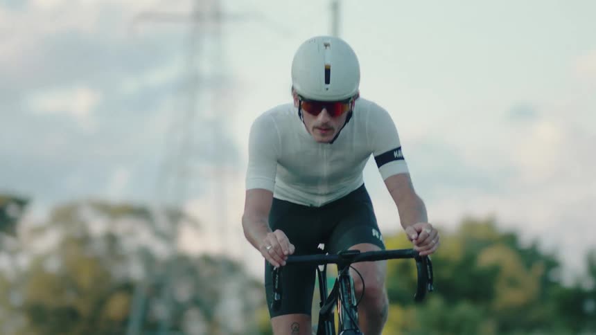 A man wearing sunglasses and a helmet is riding a bicycle on a road lined with trees