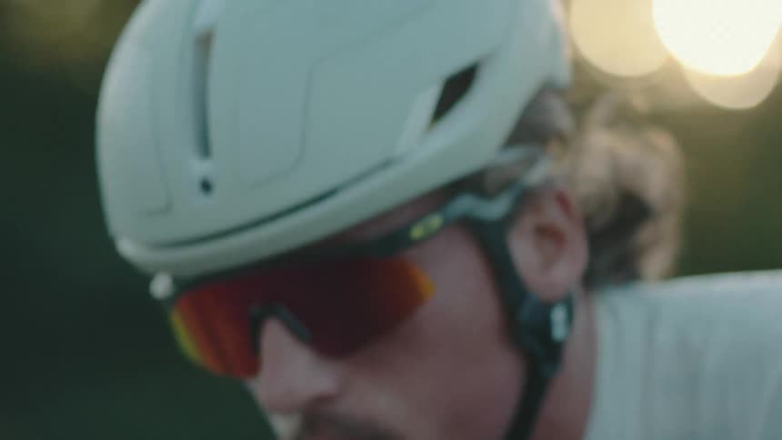 Male cyclist pedals along street passing fields on a sunny day