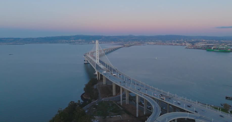 Aerial panorama of a bridge over the sea with cars moving under a pinkish dawn sky