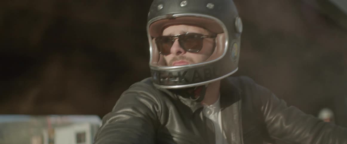 A man wearing a motorcycle helmet turns his head as smoke billows up around him