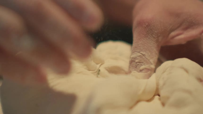 Closeup of an adult kneading bread dough in slow motion