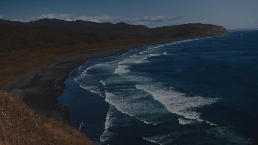 Waves roll toward dark sandy beach on a cloudy day