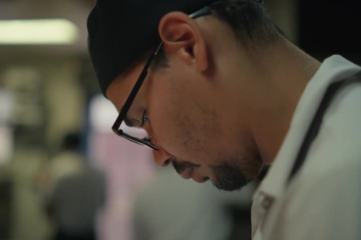 A man wearing reading glasses is counting something on paper using a pen