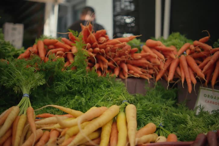 Organic carrots in various colors sit on outdoor market table near building